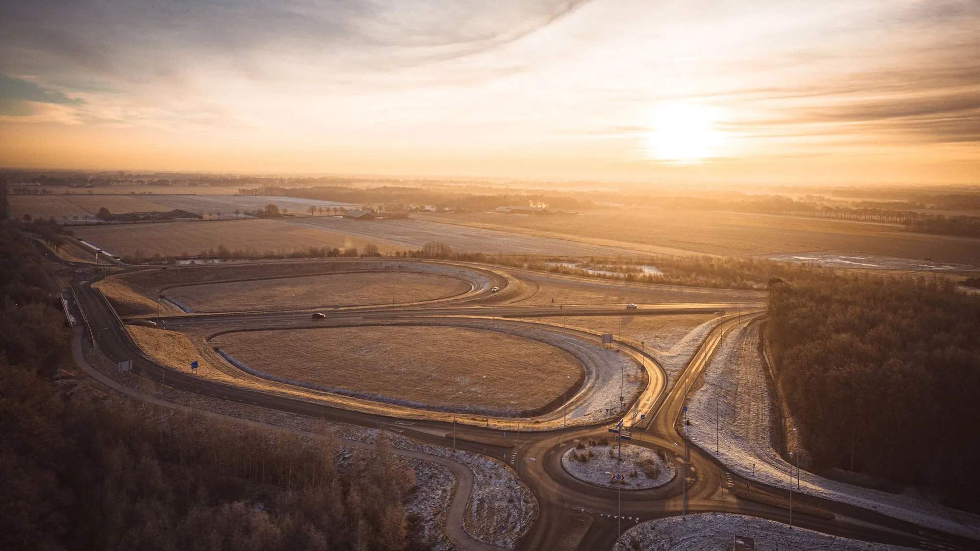 Aerial view of a highway interchange and roundabout among frosted fields at sunrise