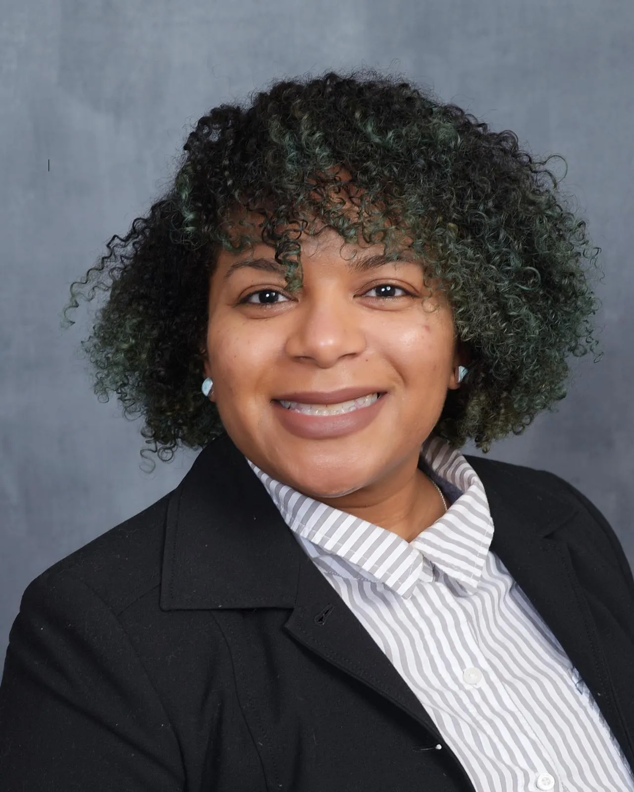 Sevil H. Modeste, licensed clinical social worker, in a black blazer and striped shirt against a grey studio backdrop
