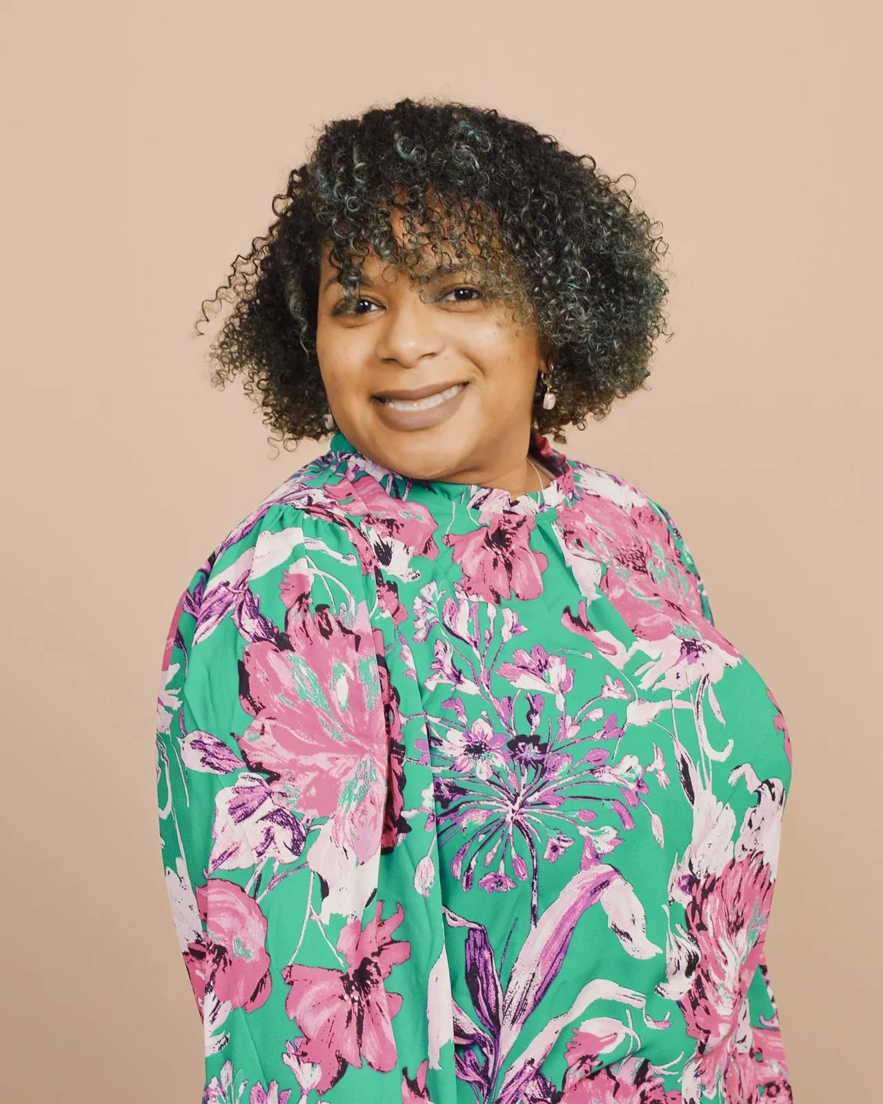 Sevil H. Modeste, LCSW, LCADC, smiling in a green and pink floral blouse against a peach studio backdrop